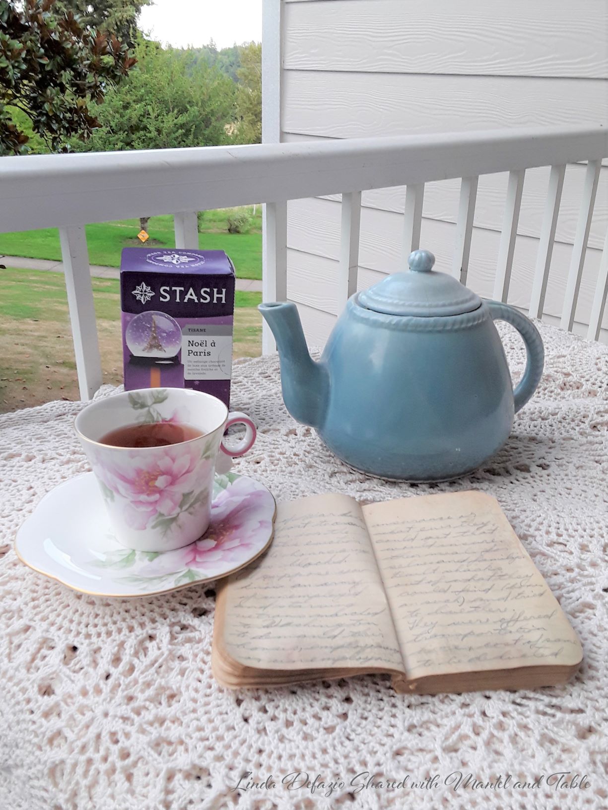 Pink flowered teacup on table with lace cloth, teapot, tea, and notebook