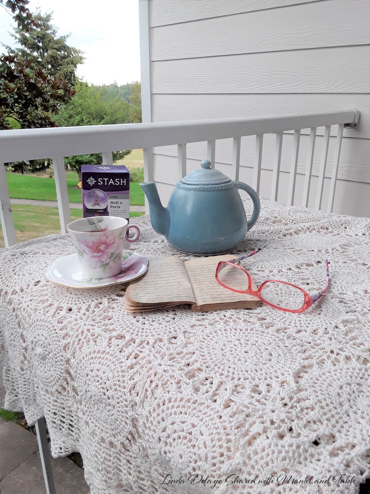 Somerset Lodge. Teacup on table with lace cloth, teapot, tea box, reading glasses and notebook