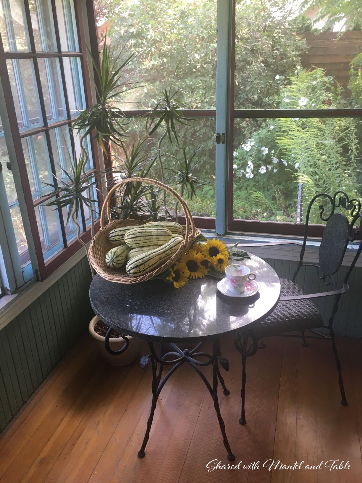 Bistro table and chair with teacup, basket of squash and sunflowers