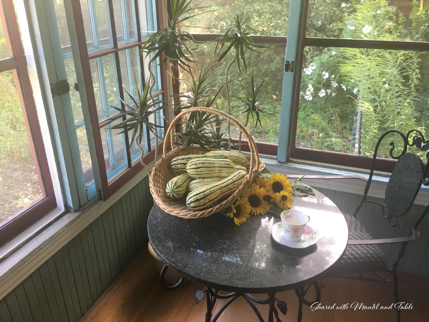 Cup on a bistro table in a sunroom with a basket of squash and sunflowers
