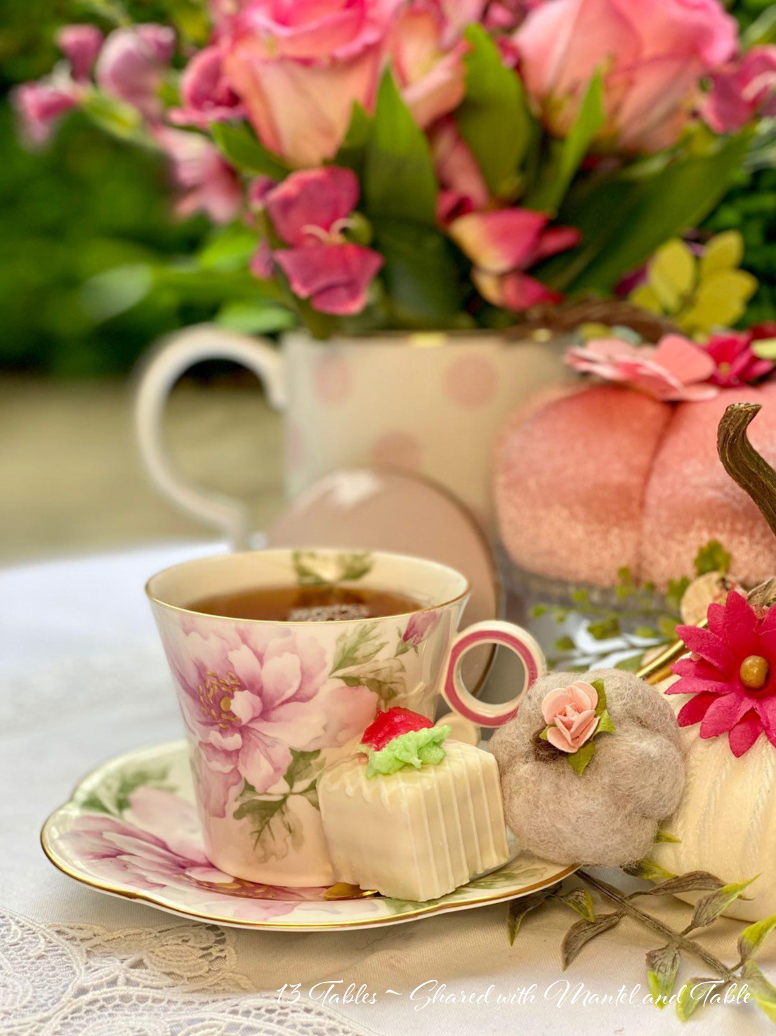 closeup of teacup & petit four, pink pumpkin in background