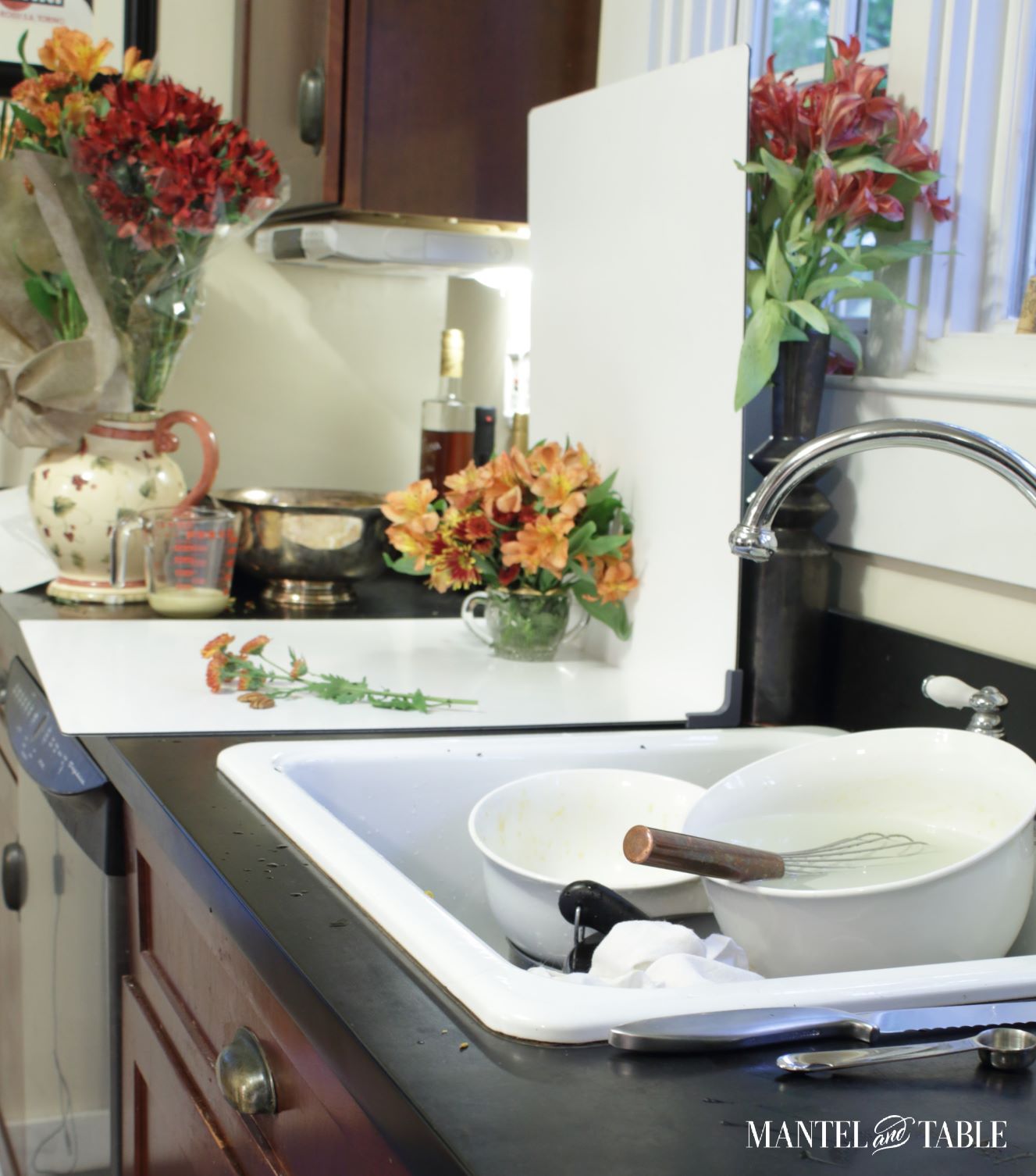 kitchen sink full of mixing bowls. white photo panels and flowers on the counter