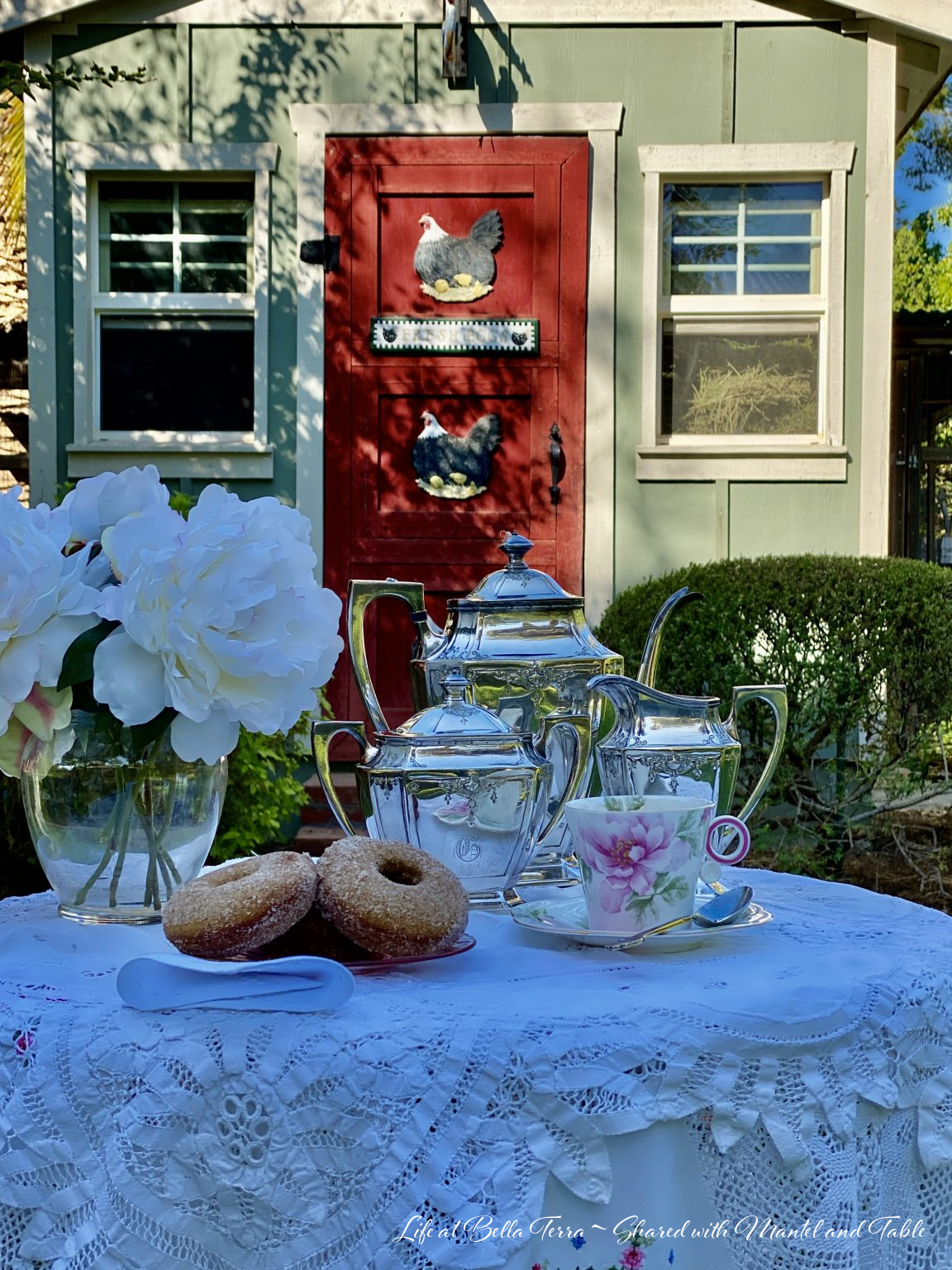 teacup on a table with flowers & silver. Chicken coop on historic estate behind.