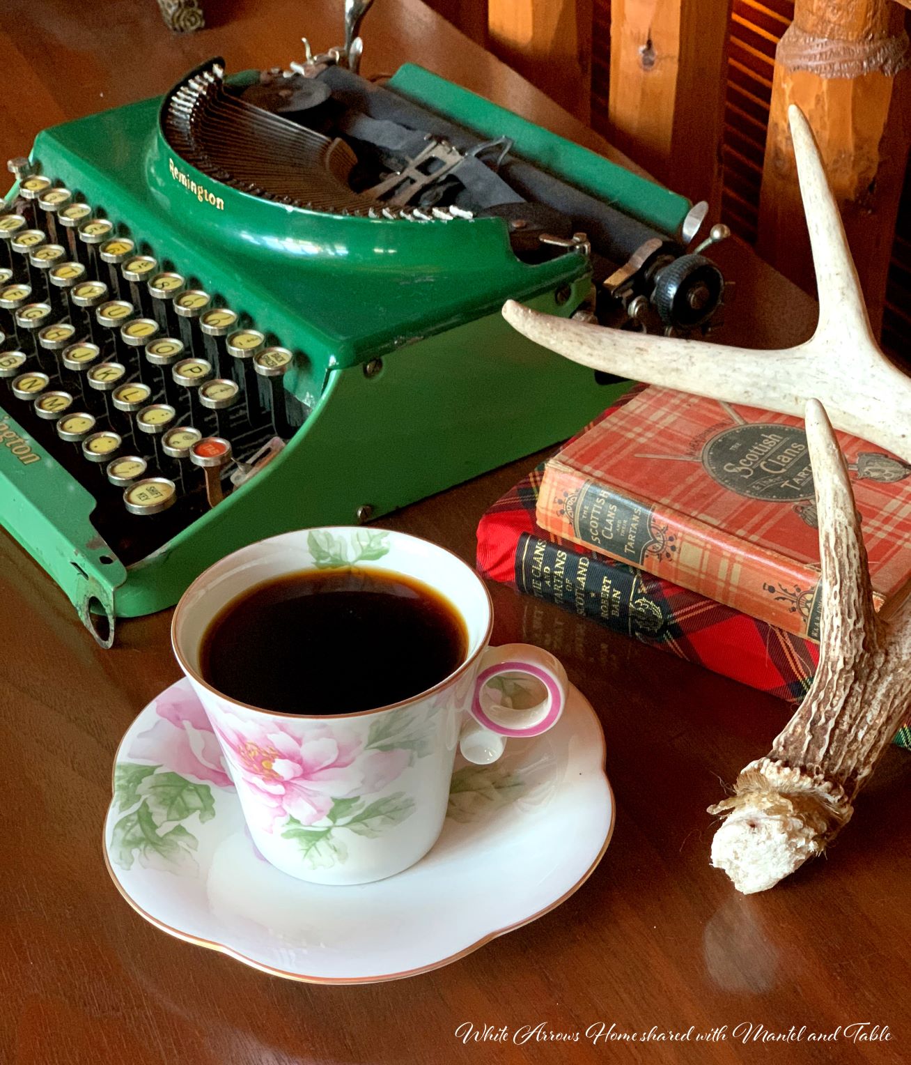 The Traveling Teacup full of coffee on table with antique typewriter, books, and antler
