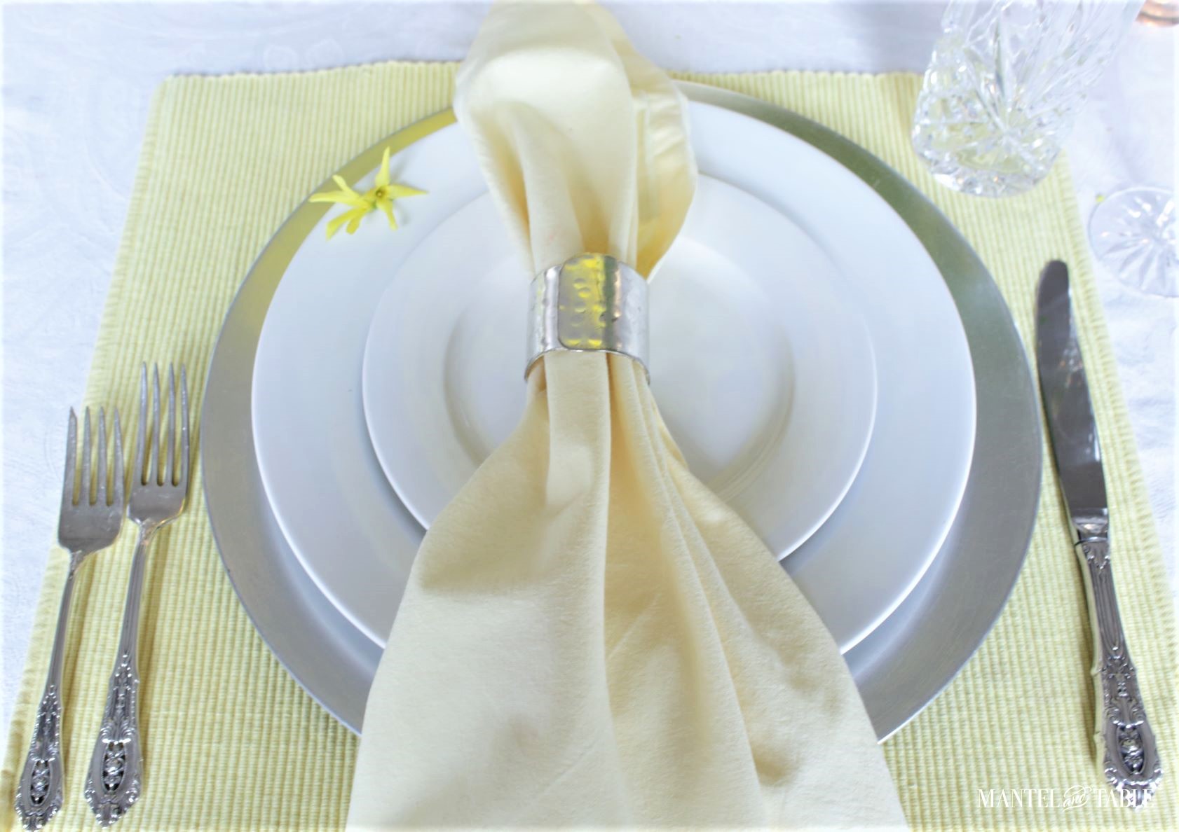 Single white and silver place setting on yellow placemat and white tablecloth