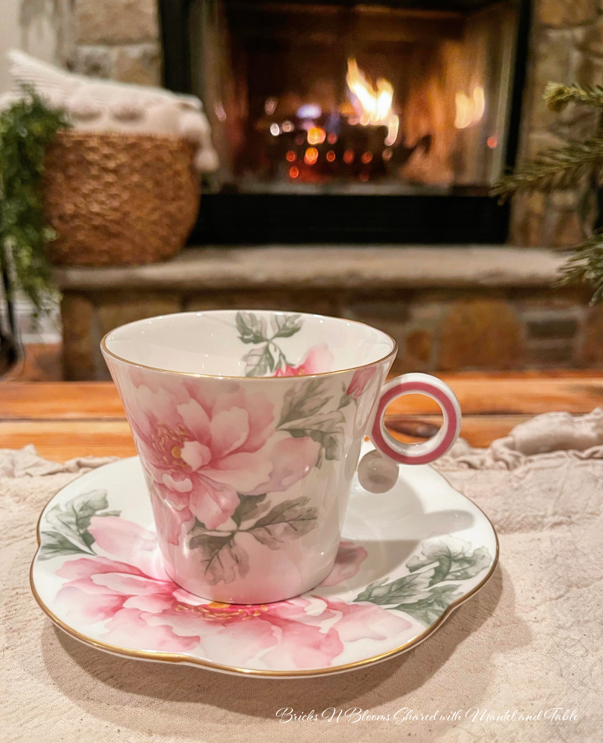Pink flowered teacup in front of a stone hearth with a fire