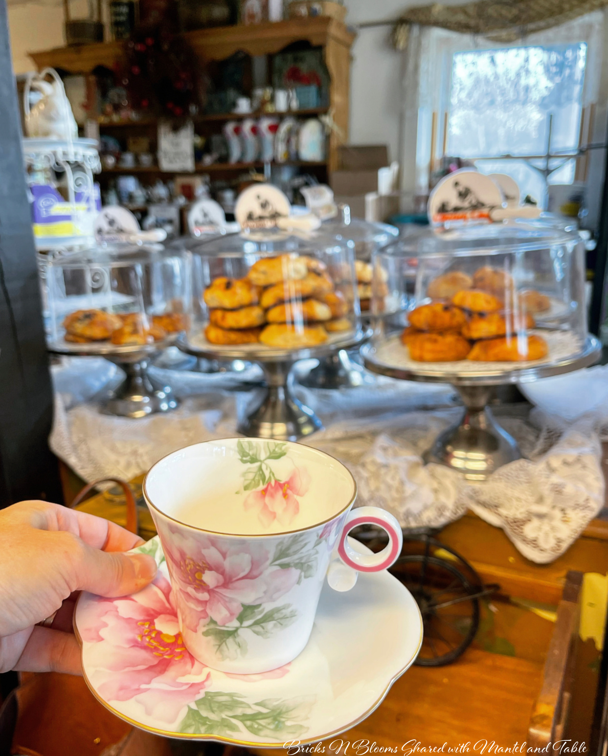 Pink and white flowered teacup in tea shop with covered plates of baked goods