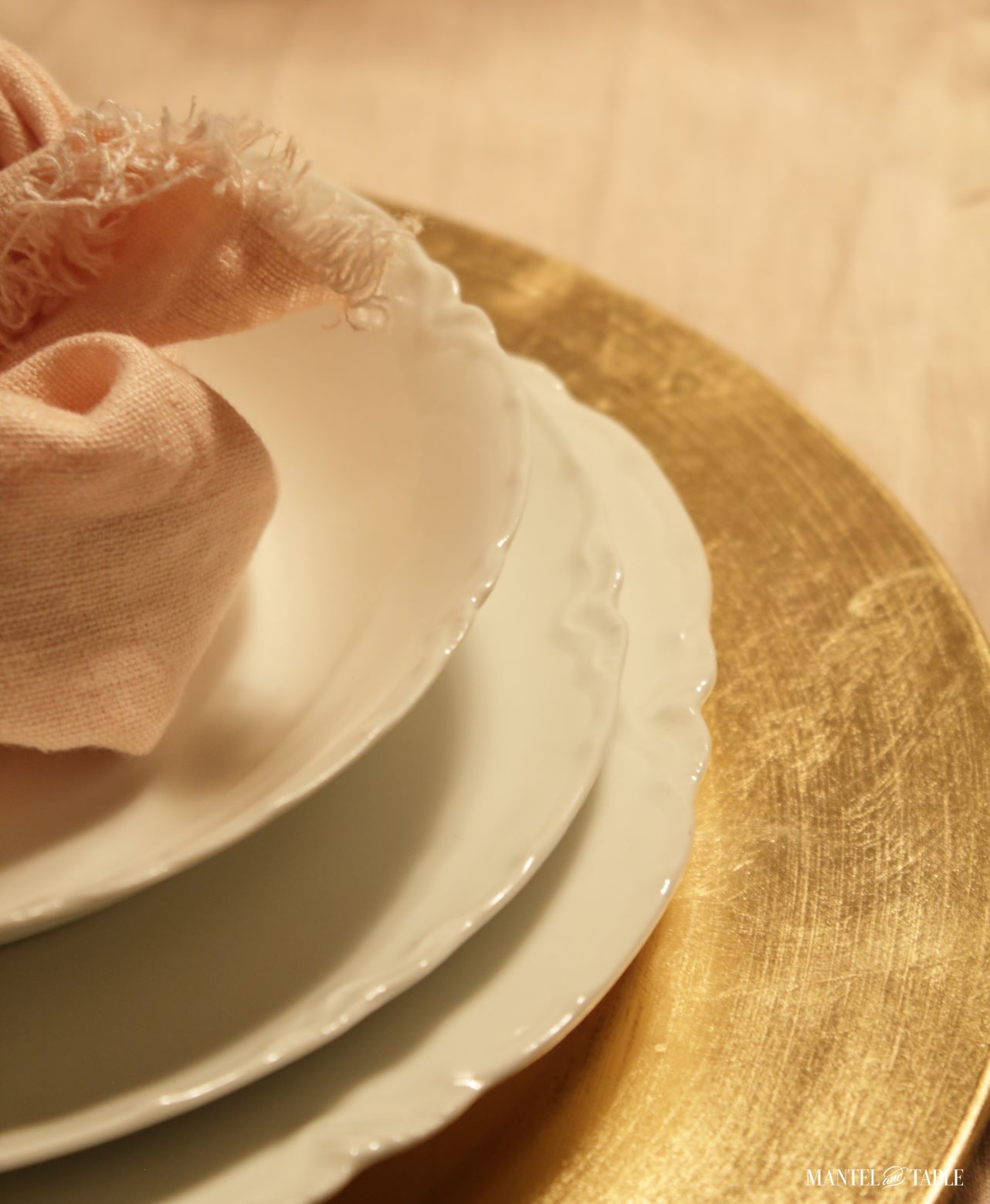 Closeup of white plate stack on gold charger with blush napkin