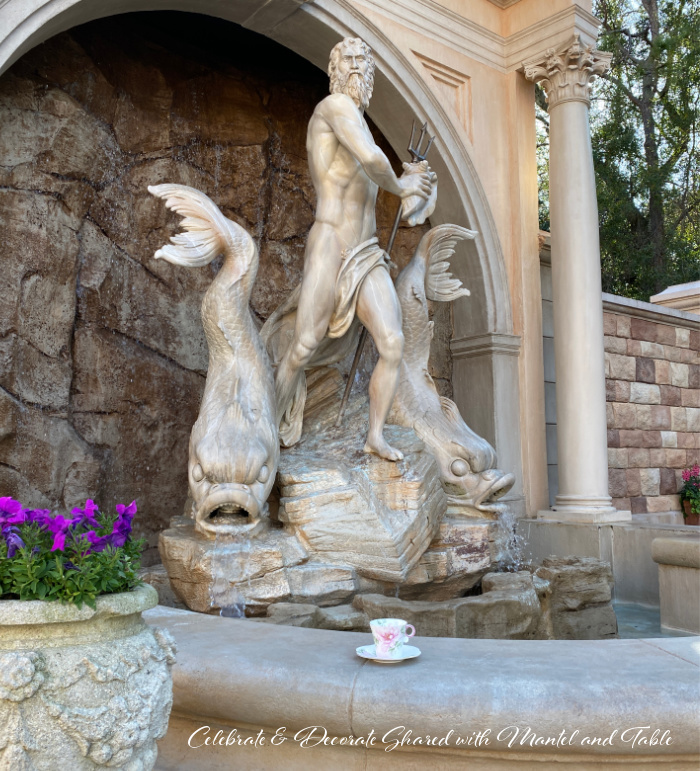 Teacup and saucer on ledge in front of marble status of Poseidon and dolphins