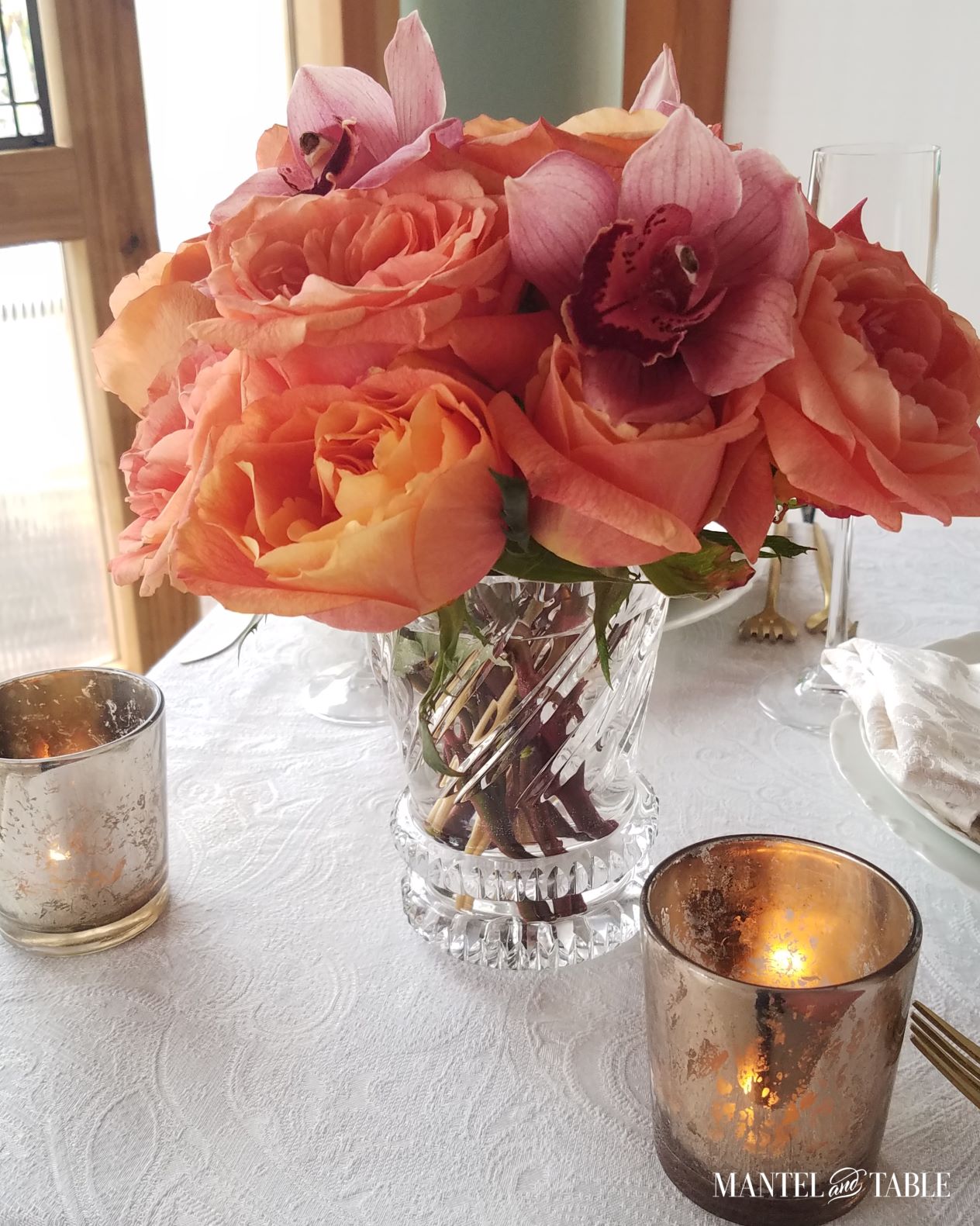 Closeup of peach/blush/yellow/orange roses and pink orchid arrangement in crystal vase