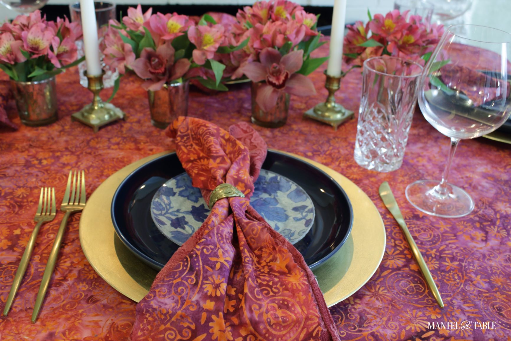 Closeup of blue and gold place setting on bright tablescape of red batik and flowers