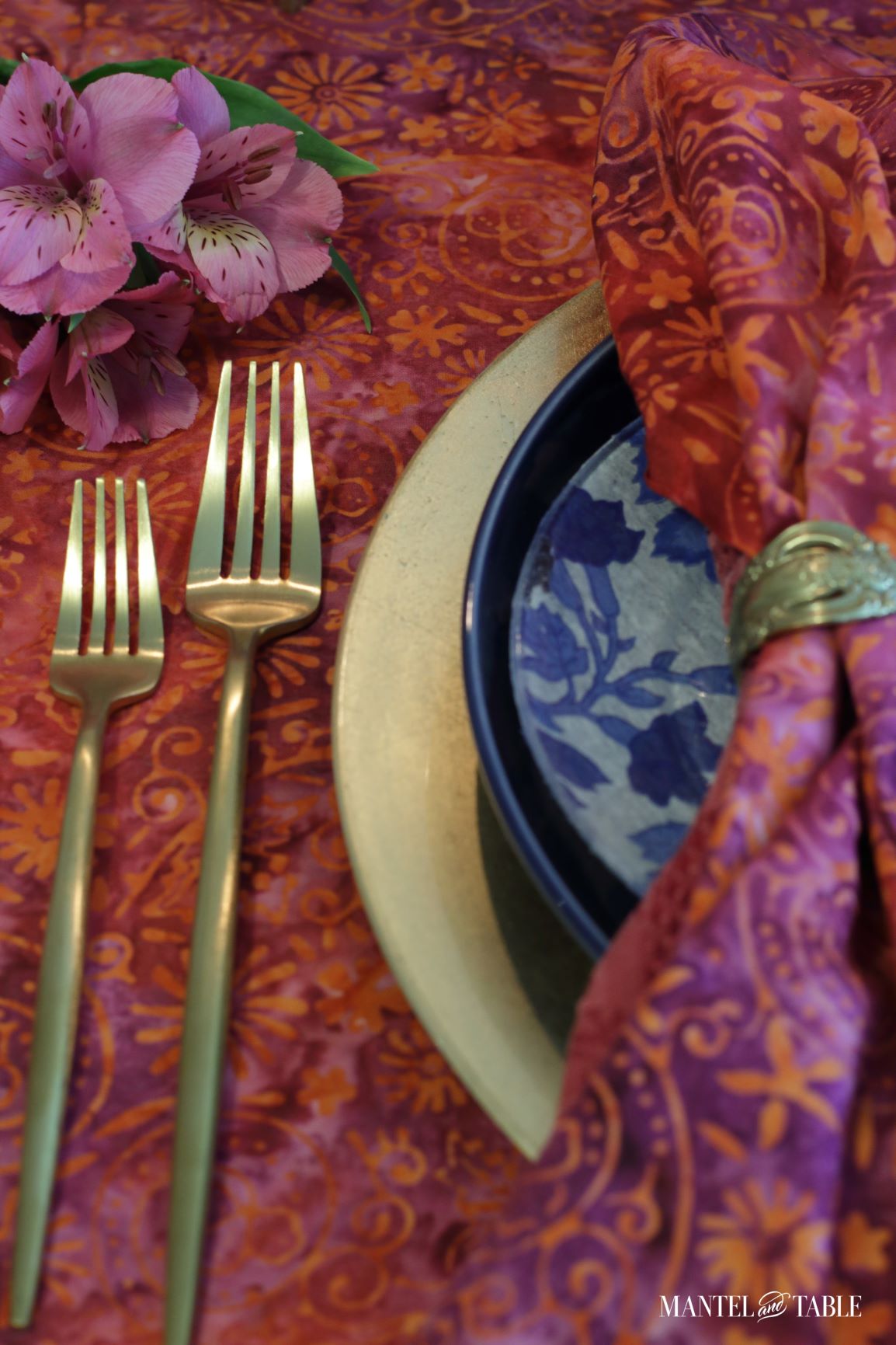 Closeup of gold forks, gold and blue plates, and red batik napkin in a place setting