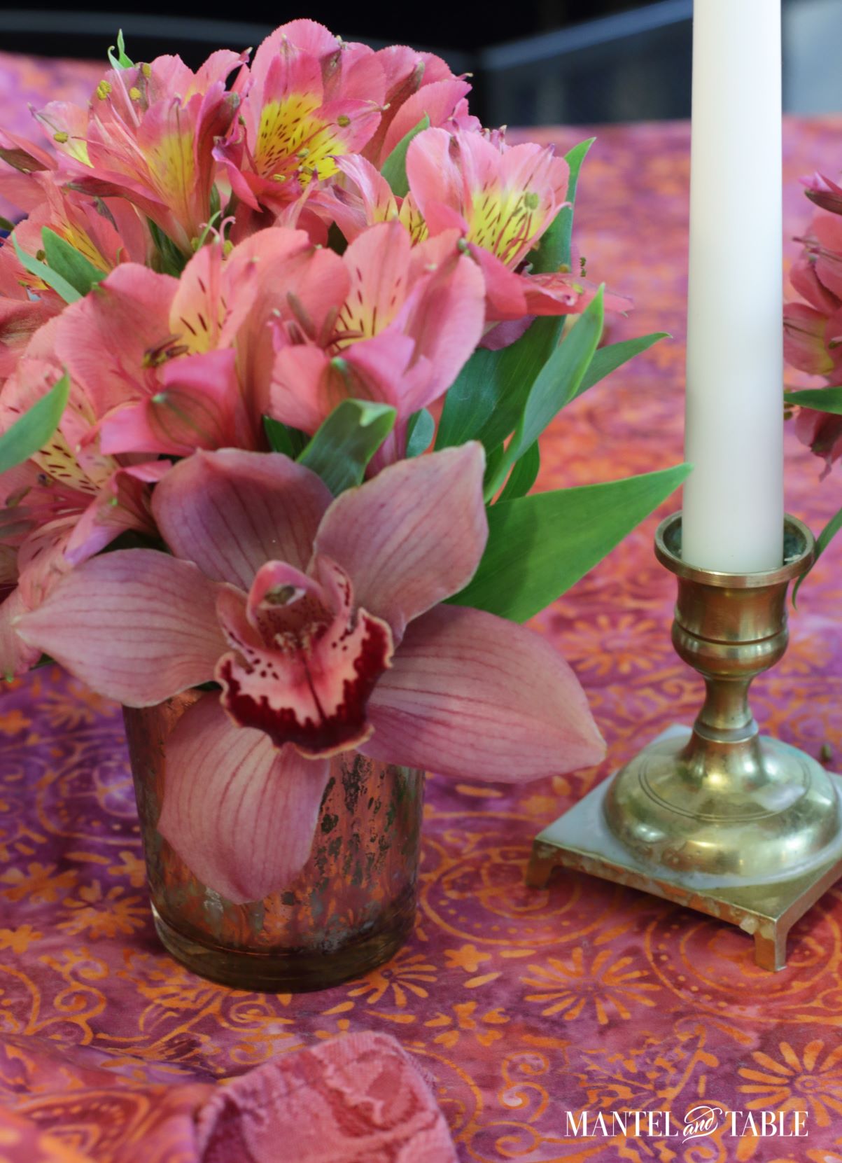 Closeup of pink-hued alstroemeria and orchid, with white taper candle in gold holder