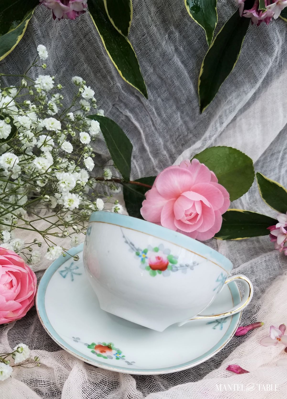 Closeup of teacup lying on its side on the saucer. Pink spring flowers around it