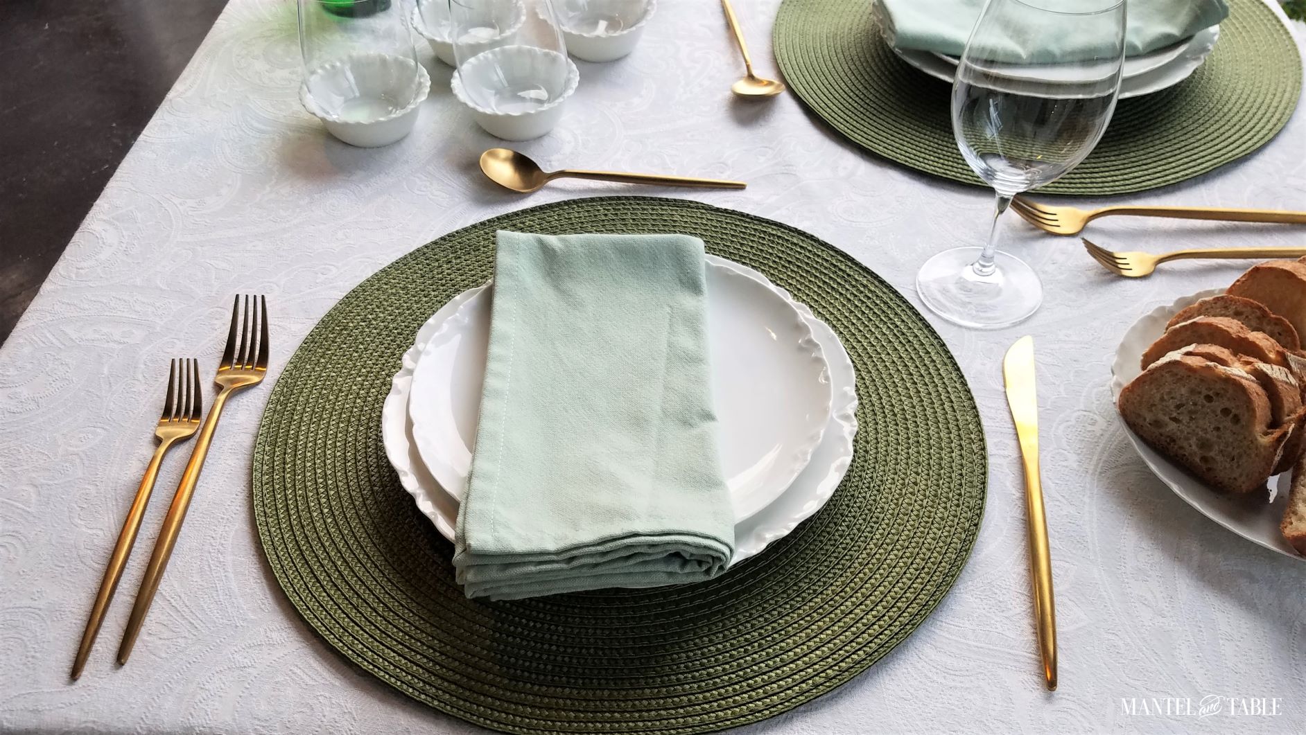 Olive green and white place setting from above. White plates, gold flatware