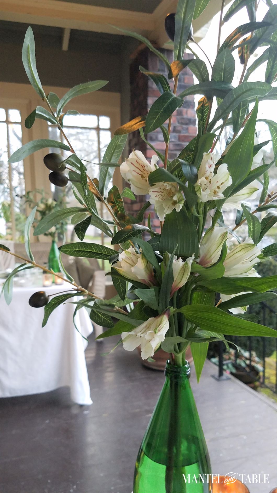 Closeup of flower arrangement - white alstroemeria and faux olive branch in green bottle