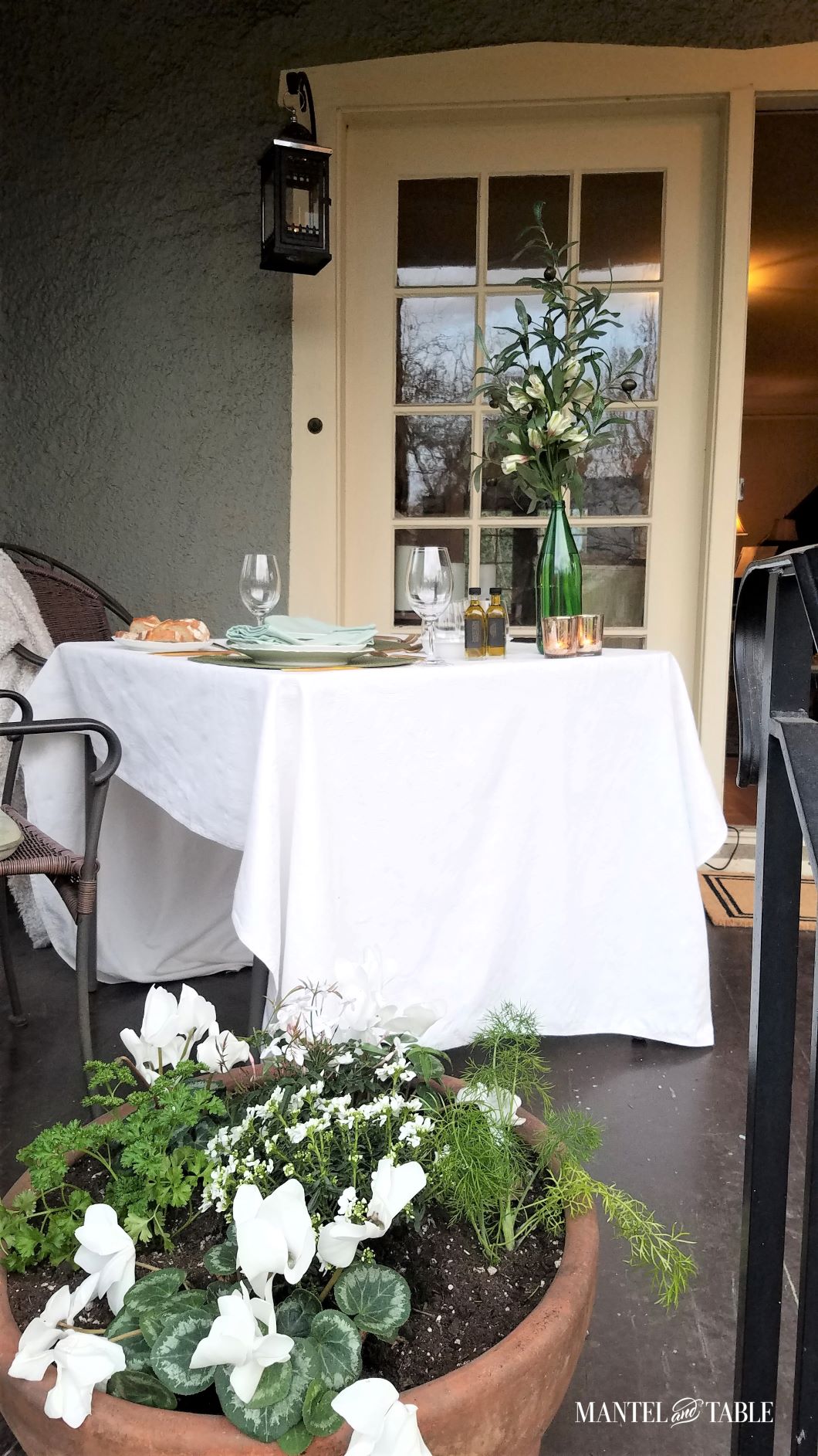 Side view of green and white table on porch, white flowers in planter in the foreground