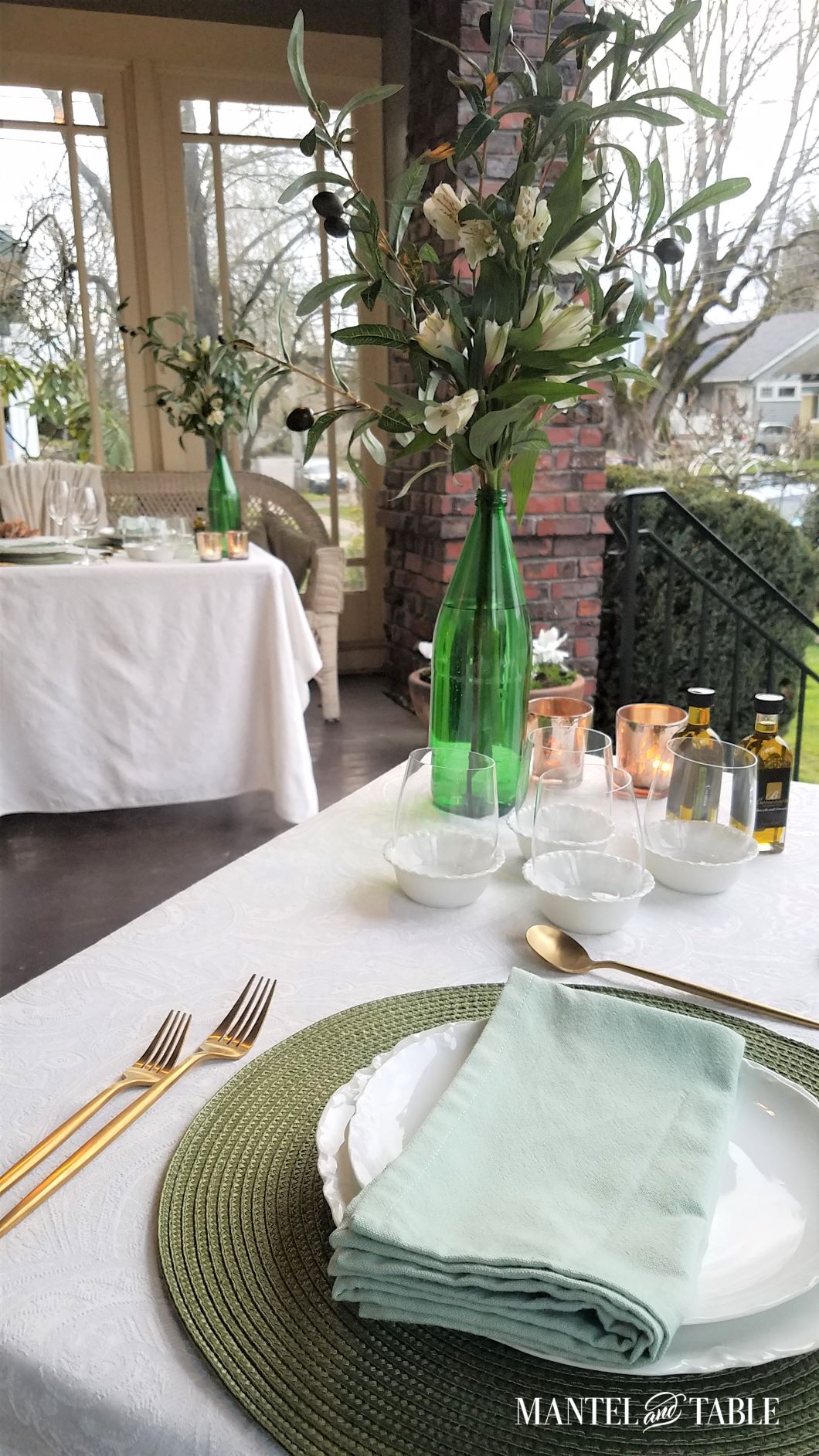 Side view across one green and white tablescape to another across the porch. White flower arrangements, and olive oil tasting setups.