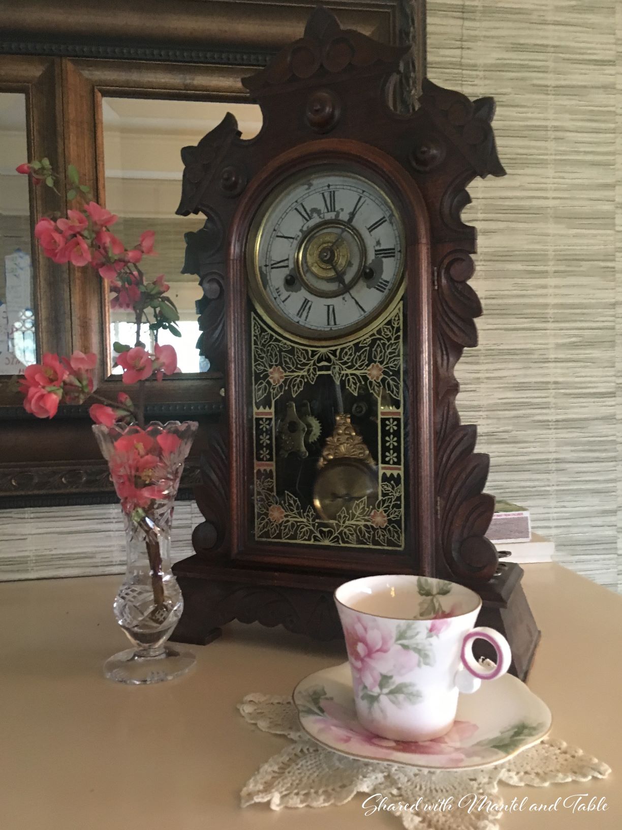 Teacup and saucer on mantel with antique mantel clock and crystal vase of pink blossoms