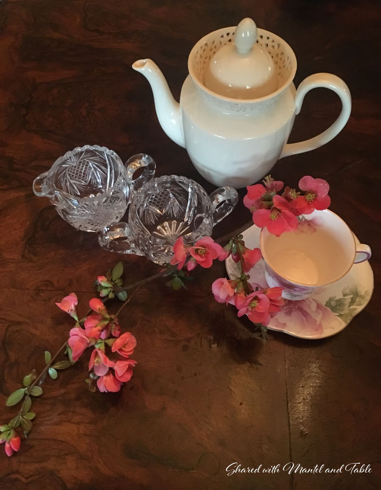 Top view of china teacup, teapot, crystal creamer & sugar, and flowering branch