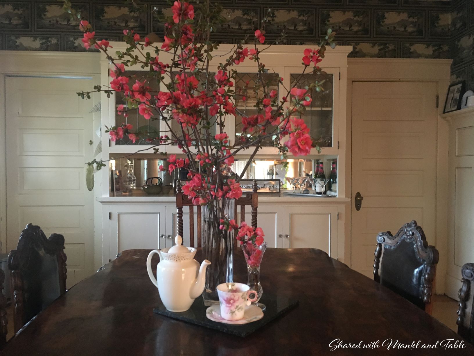 Full view of dining room featuring teacup and tall vase of flowering branches in the center of table