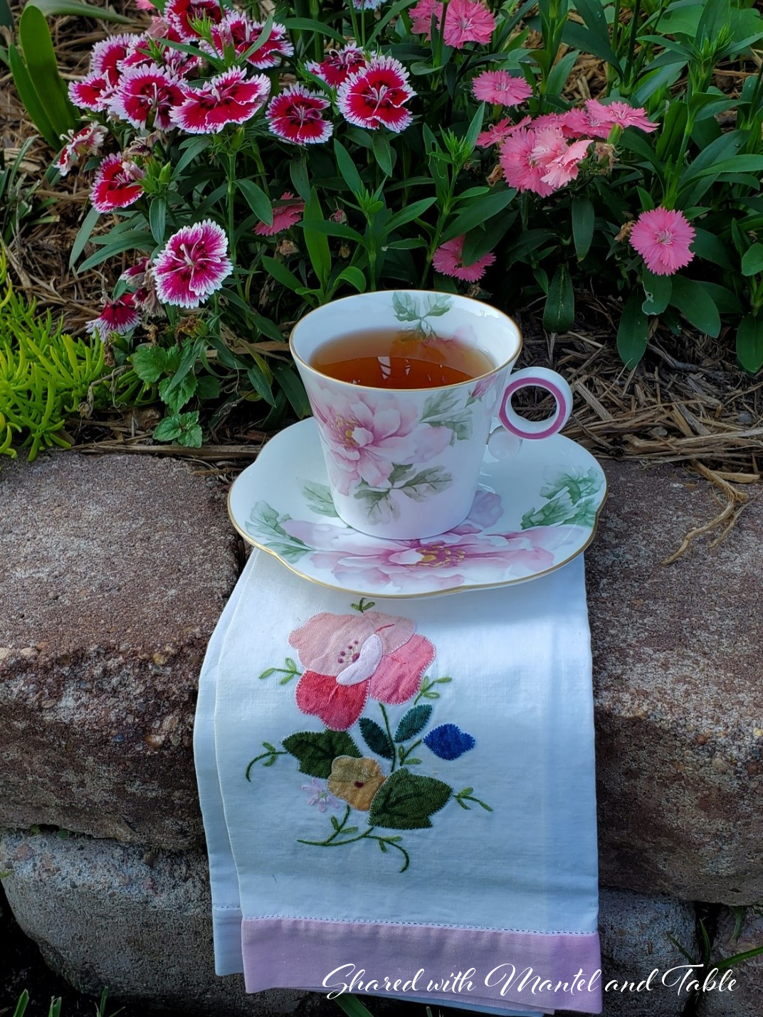 Teacup with tea, resting on embroidered tea towel on garden wall