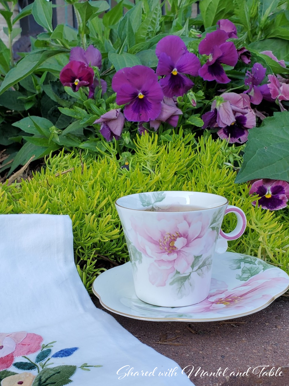 Flowered teacup with tea towel and purple flowers in a garden