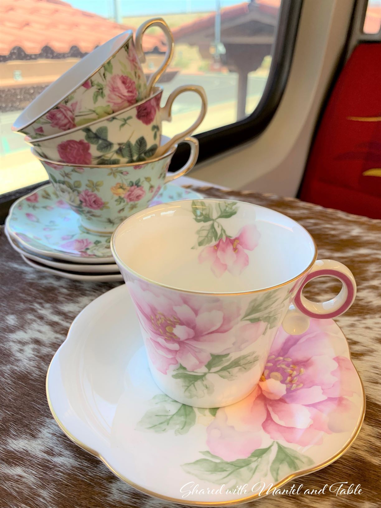 The Traveling Teacup on brown and white cowhide with delicate floral and gold teacup stack on the train tray table
