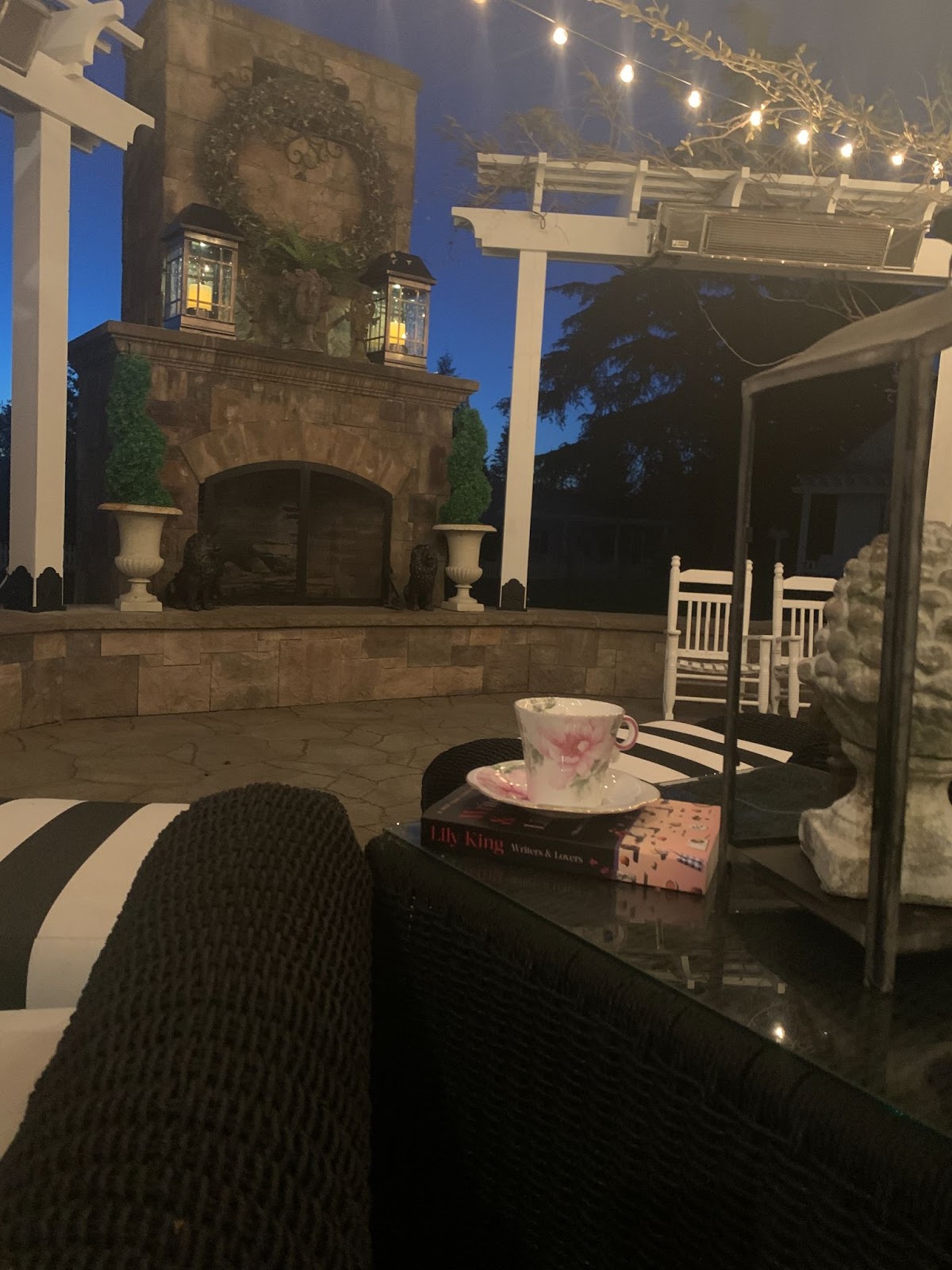 The Traveling Teacup outside on the patio at twilight resting on a book in front of stone fireplace
