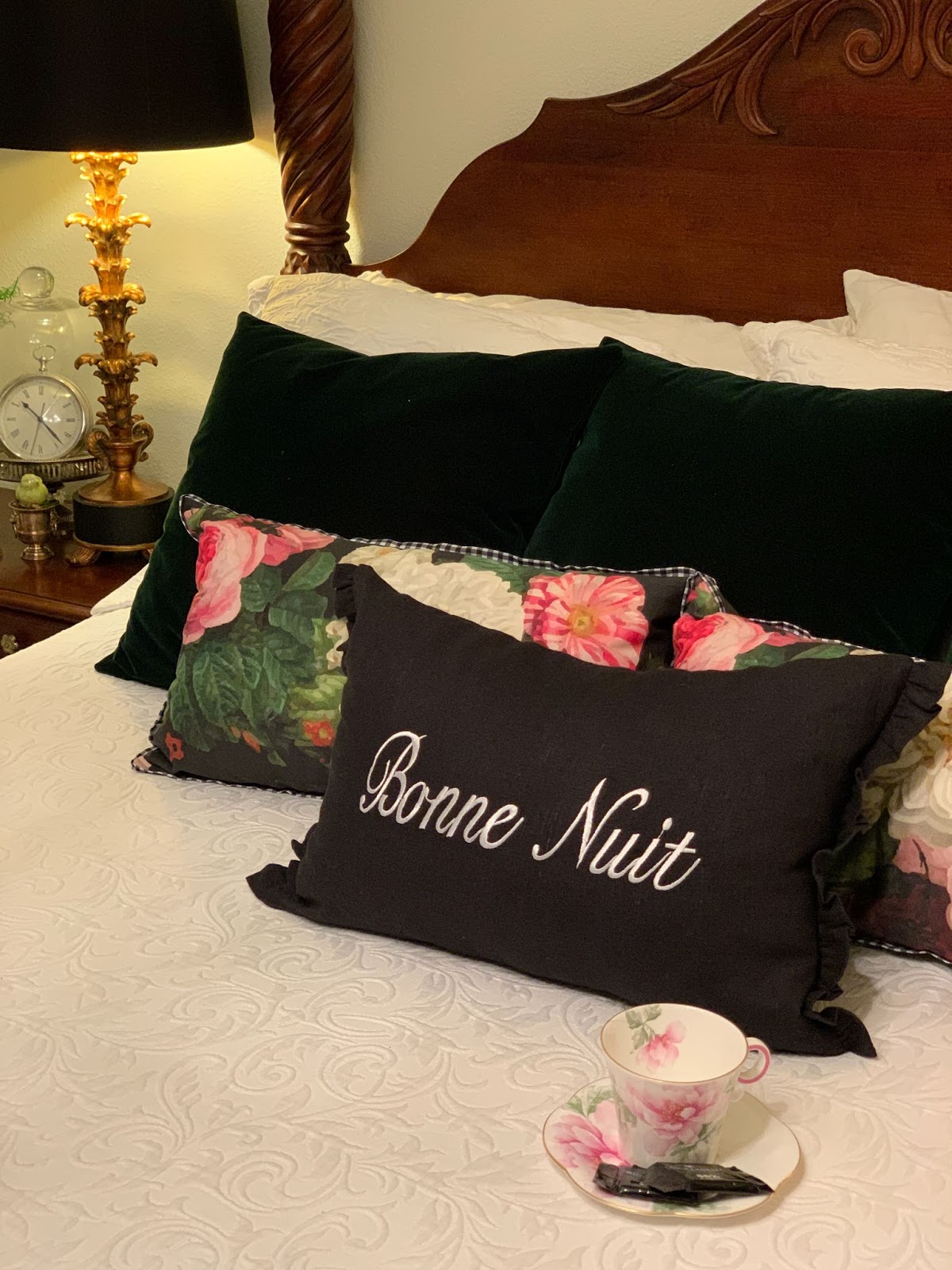 Pink and white teacup and saucer on bed with white and green linens, pink flower & "Bonne Nuit" pillows