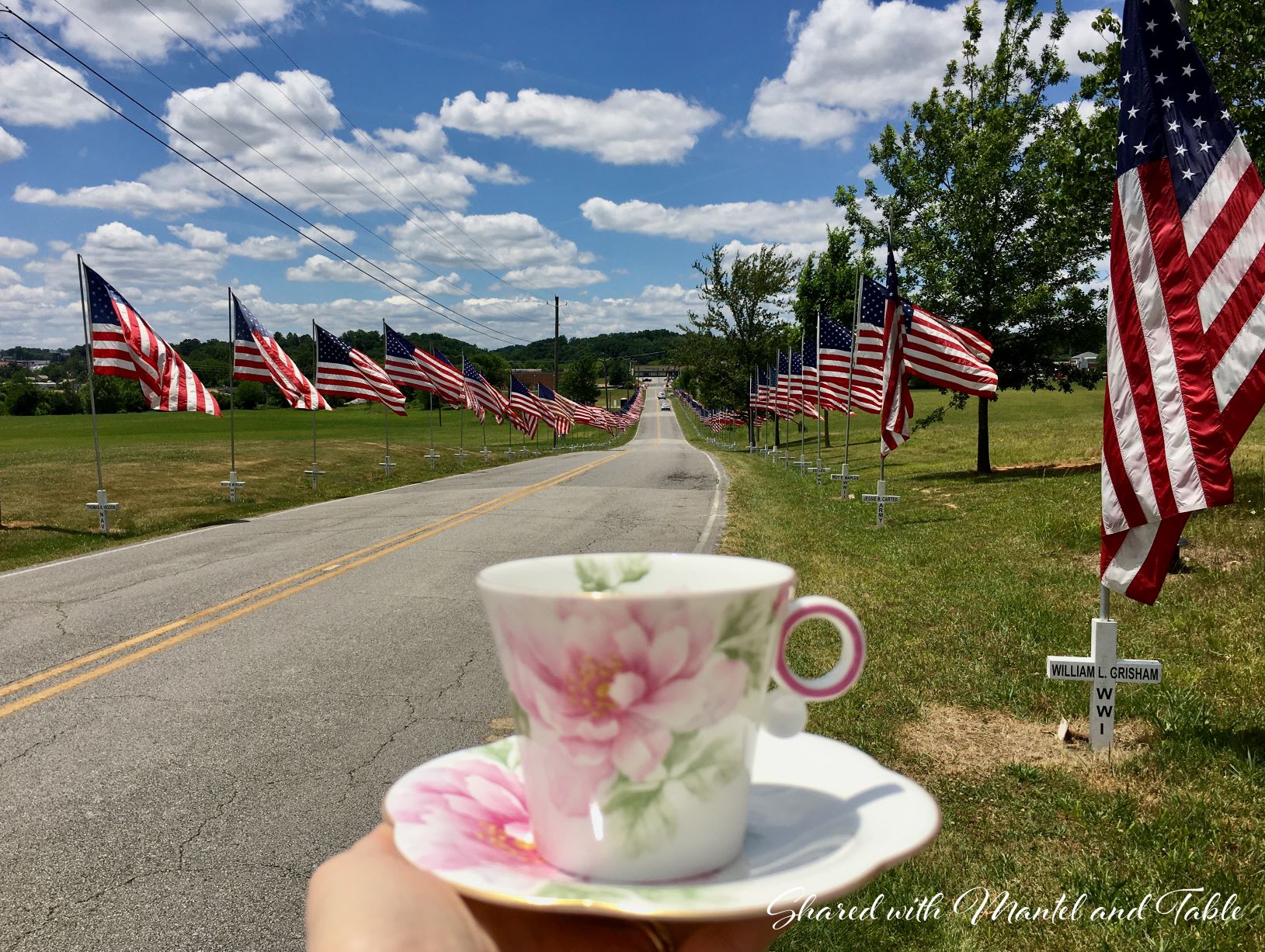 The Traveling Teacup held in hand in front of street lined with Memorial Day flags and crosses