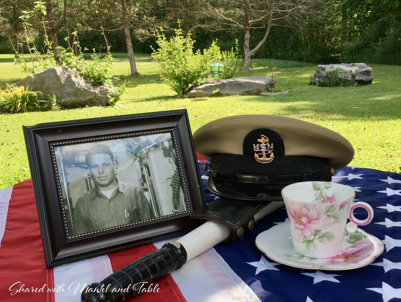 Memorial Day table draped in American flag, holding photo of soldier, Navy hat, and teacup