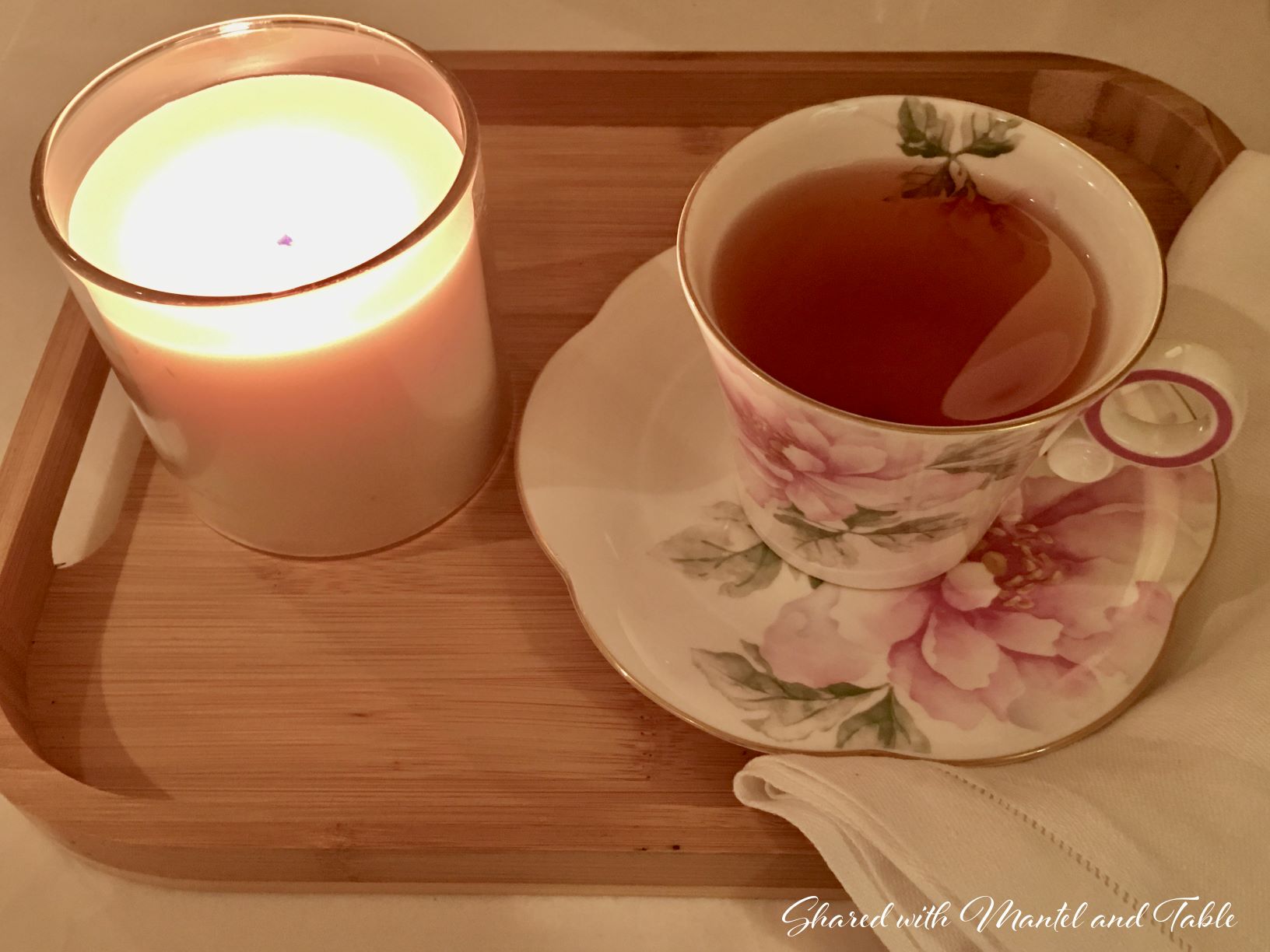 White and pink flowered teacup and saucer on tray with lighted candle