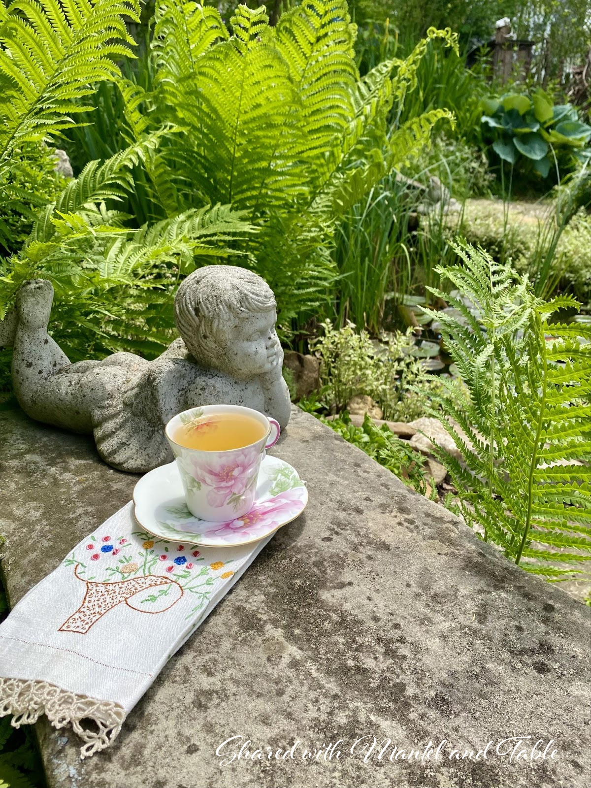 Traveling Teacup on garden wall next to cement angel, overlooking pond