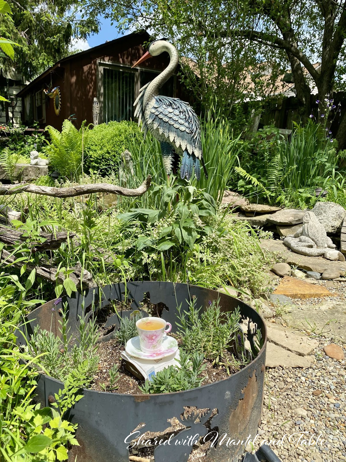 Tall blue heron sculpture with lavender growing in firepit
