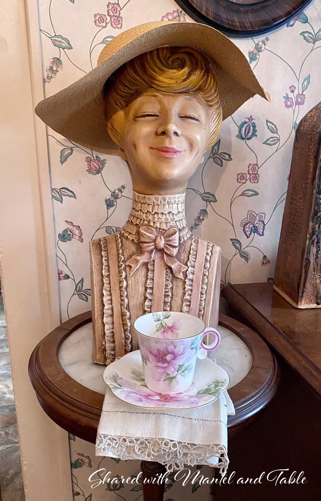 Traveling Teacup in front of a painted head statue of happy woman wearing straw hat