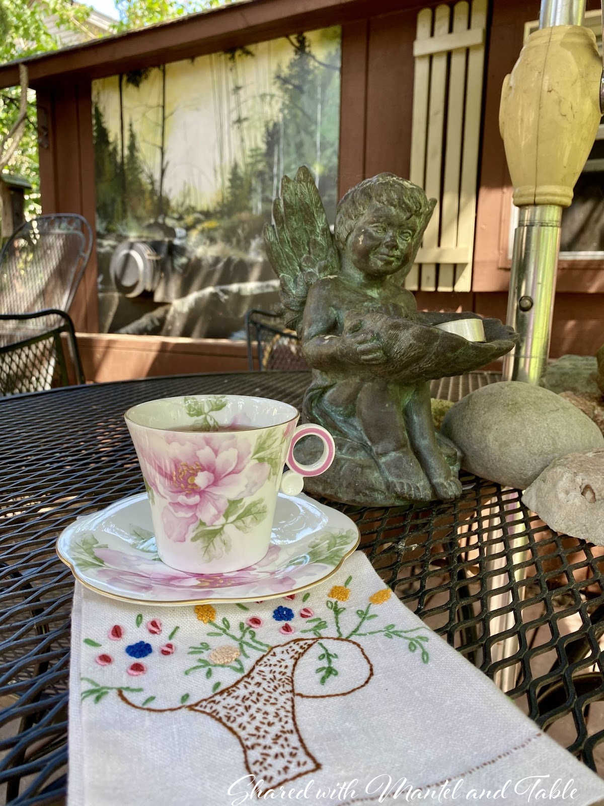 The Traveling Teacup on black garden table with cherub statue