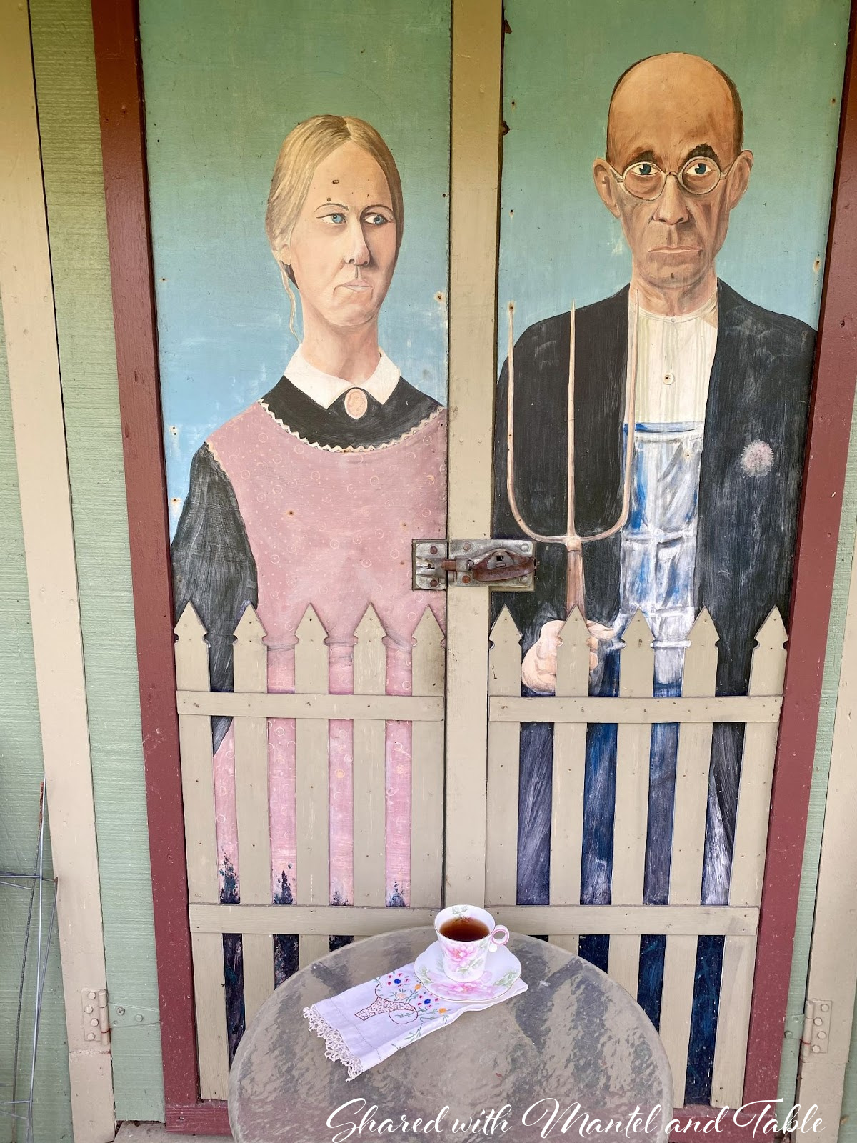 Reproduction of American Gothic painting on shed doors. Teacup in foreground
