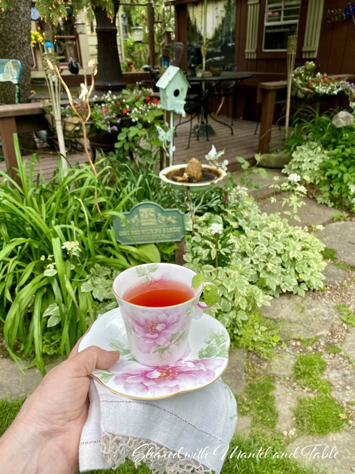 Hand holding the Traveling Teacup in front of a garden with Certified Wildlife Habitat sign