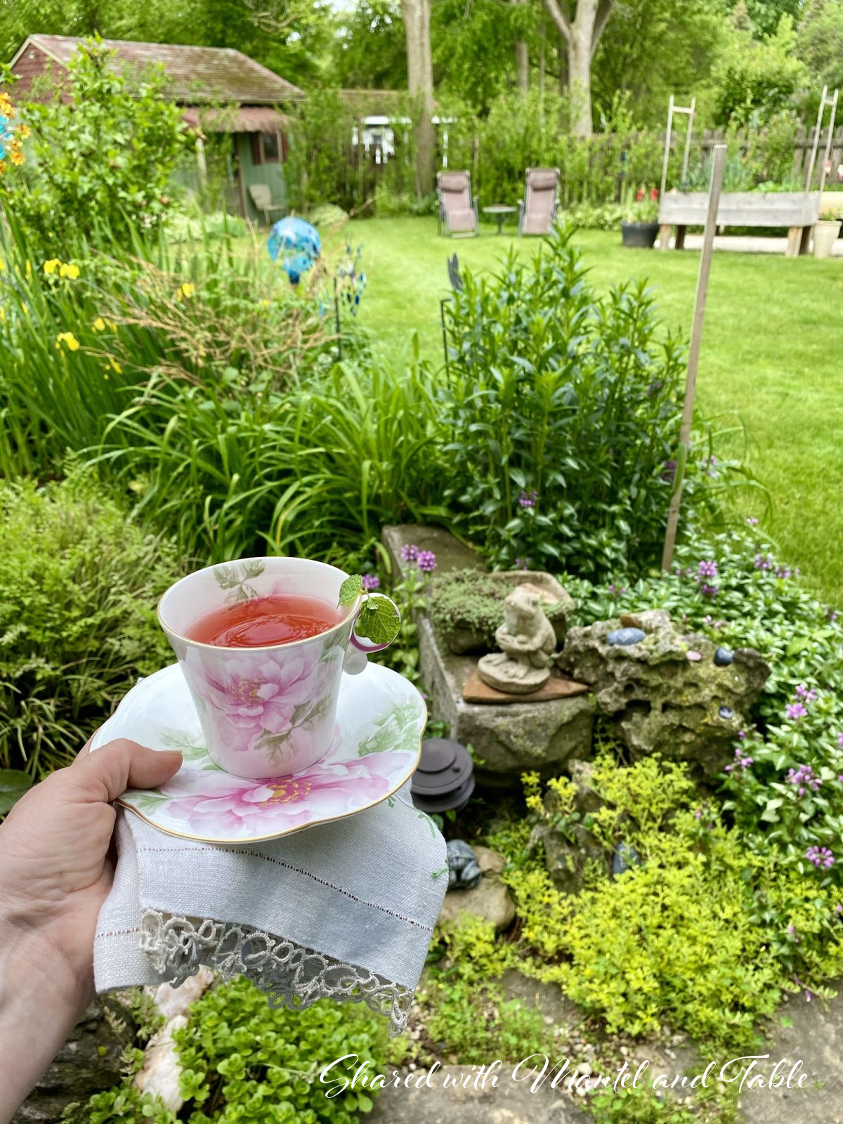 View into the yard, hand holding teacup in the foreground