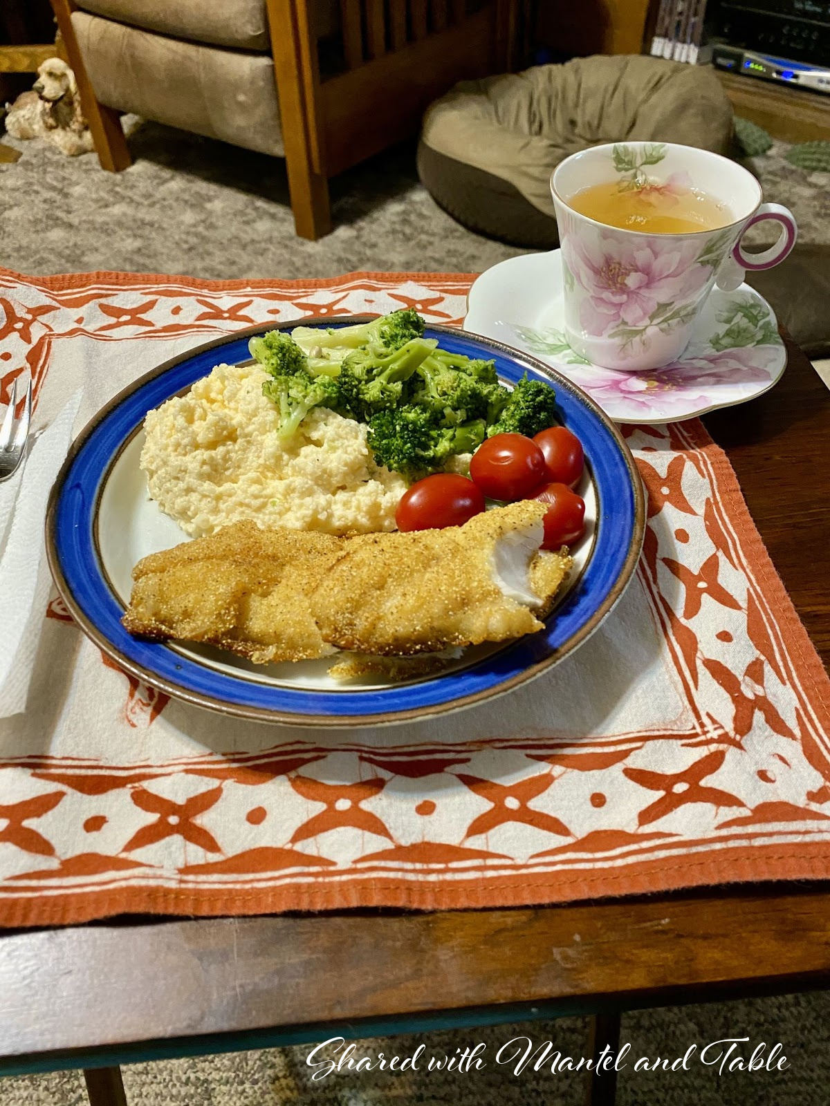 Plate of dinner on tray table with teacup full of tea. Cavalier spaniel in the background