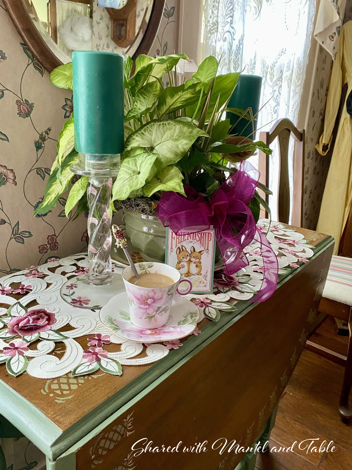 The Traveling Teacup on a side table with green plants, candles, and Friendship sign