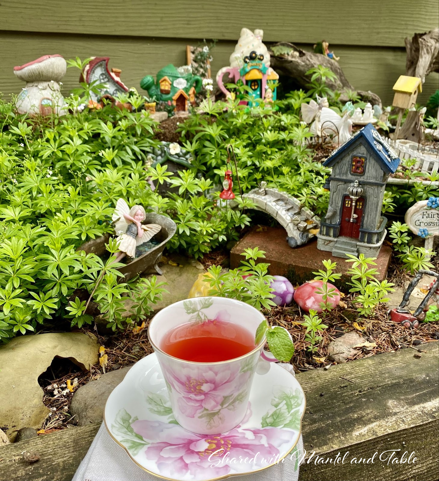 The Traveling Teacup on the border of garden with miniature fairy village statuettes