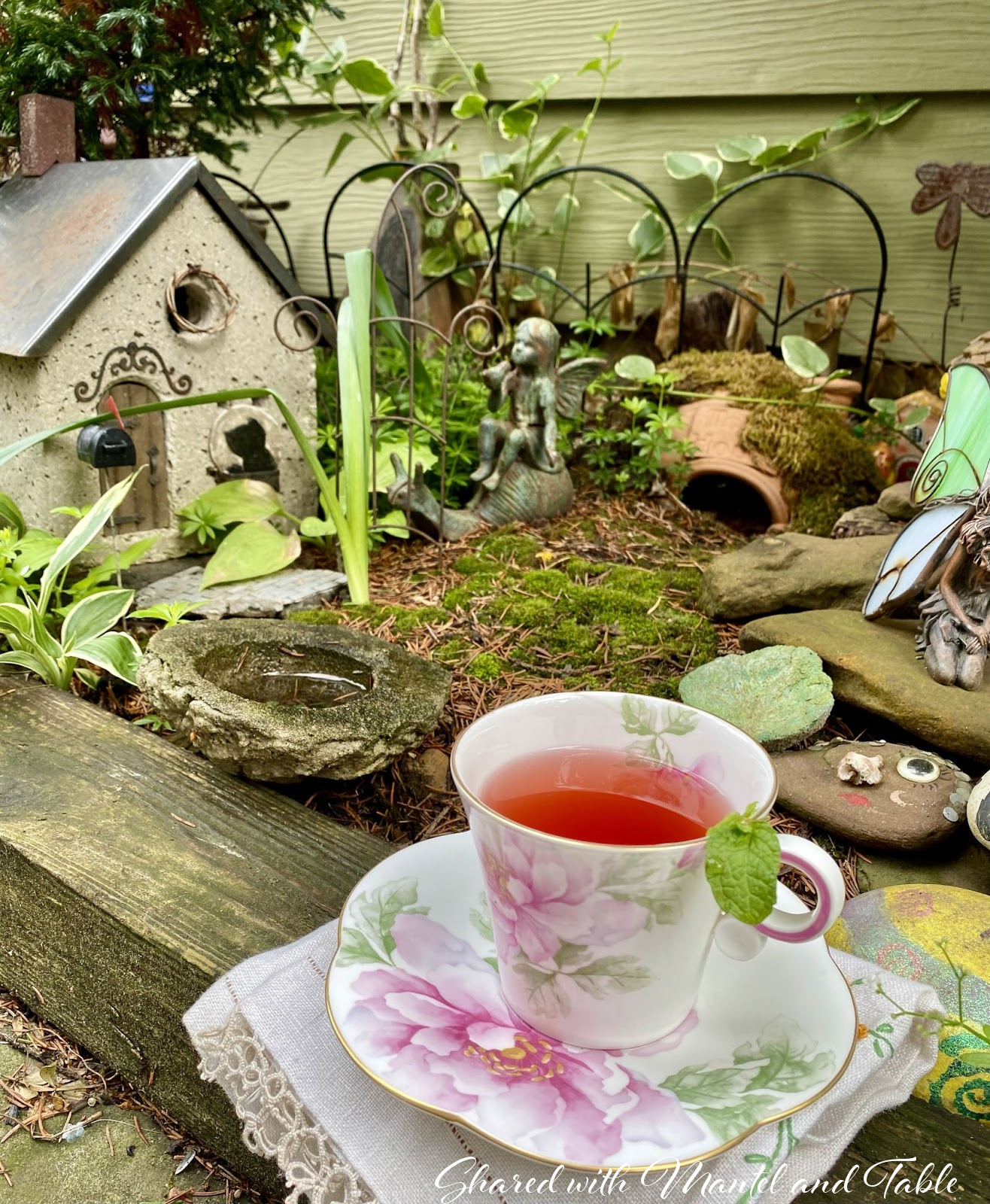 Closeup view of fairy garden. Teacup in foreground with a mint sprig over the rim