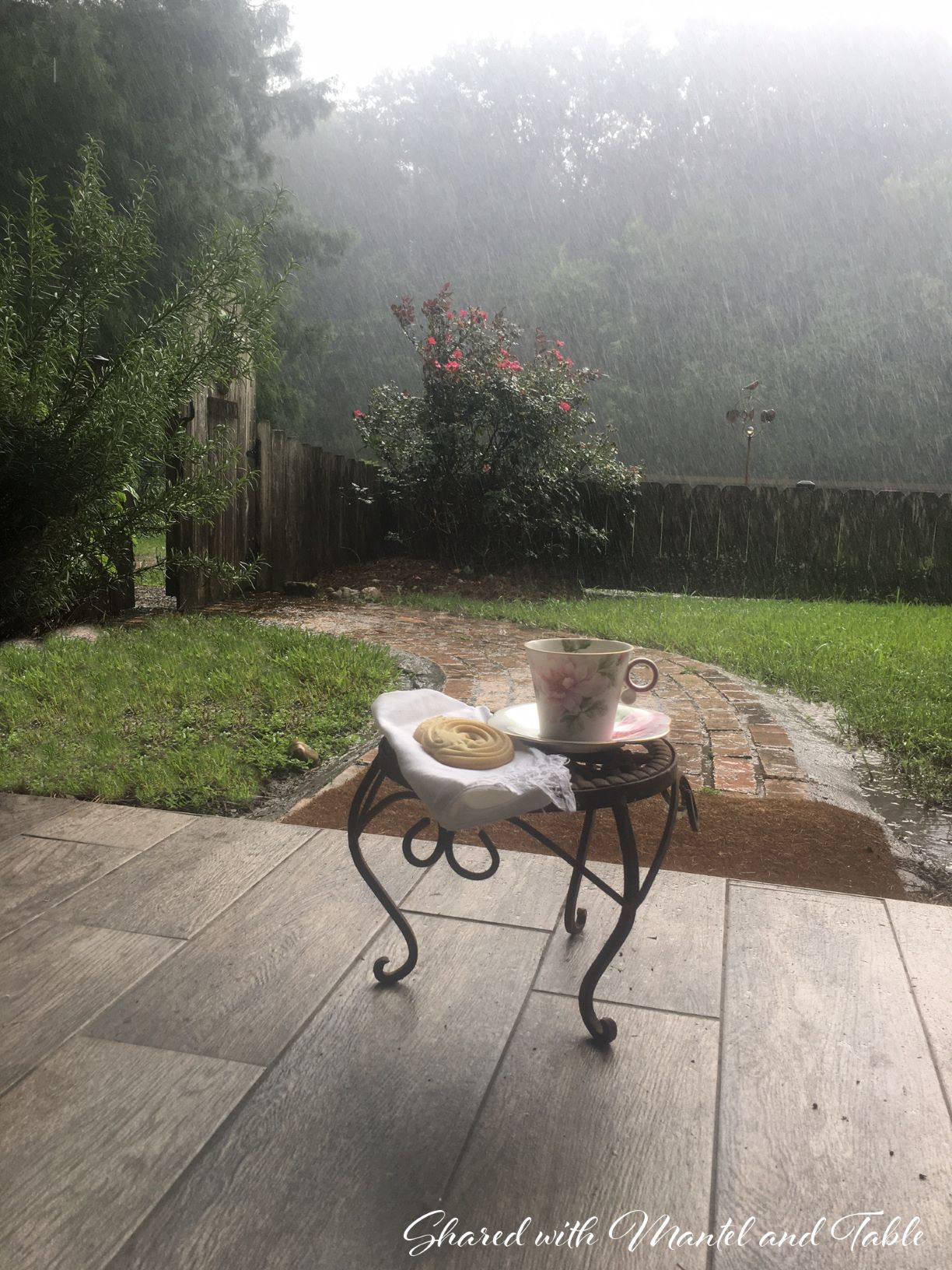 The Traveling Teacup on a little table on the porch looking into a rainy Louisiana yard. Danish on the table.