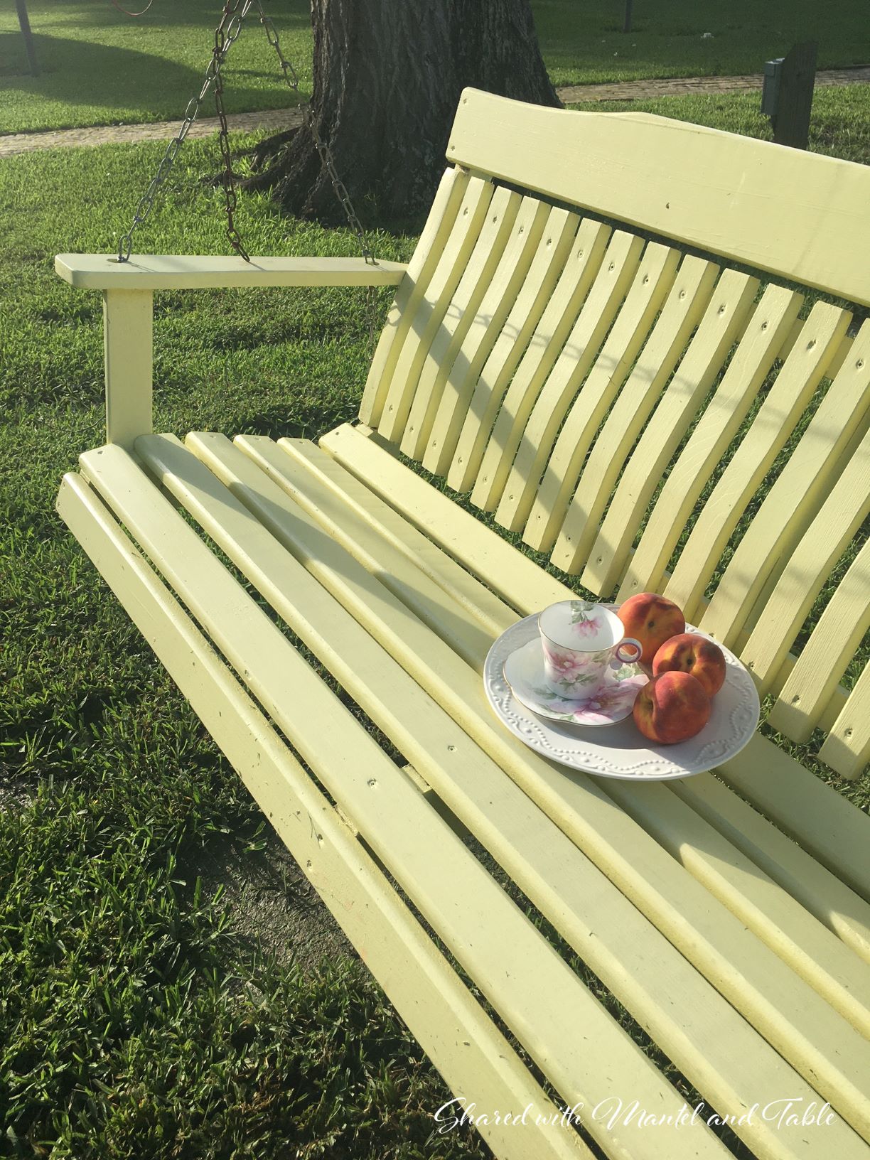 teacup, plate, peaches on a yellow garden swing surrounded by lawn and trees