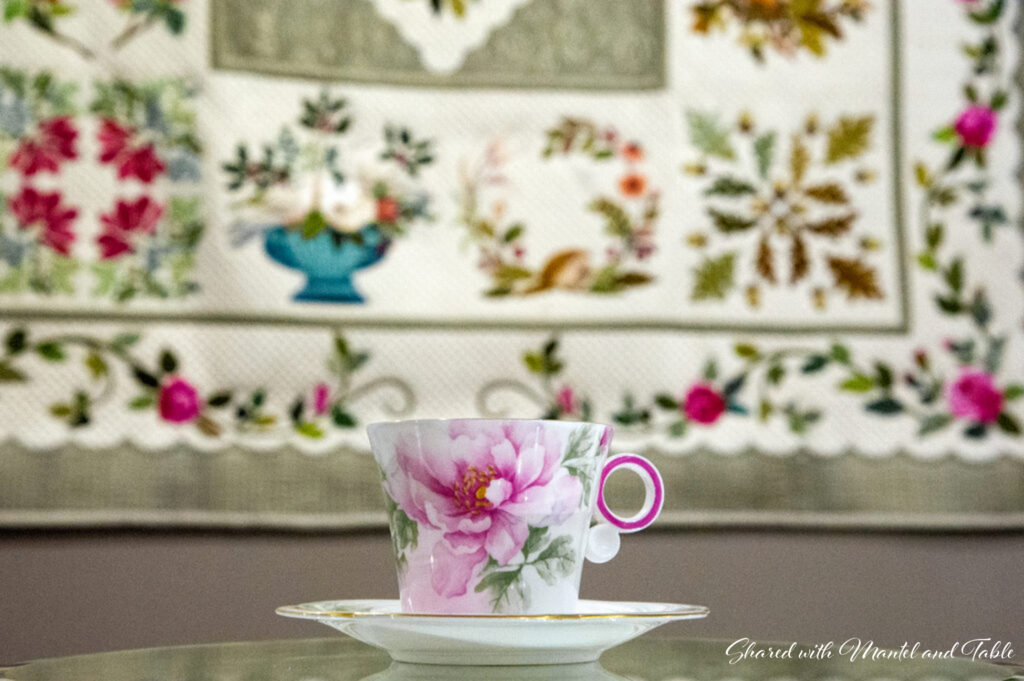Pink & white flowered teacup in front of hanging flower-bordered quilt at Paducah's National Quilt Museum