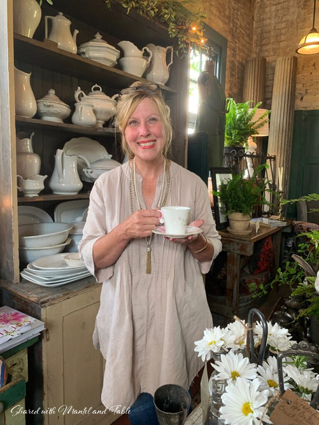 Pretty woman standing in anantique shop holding The Traveling Teacup and saucer
