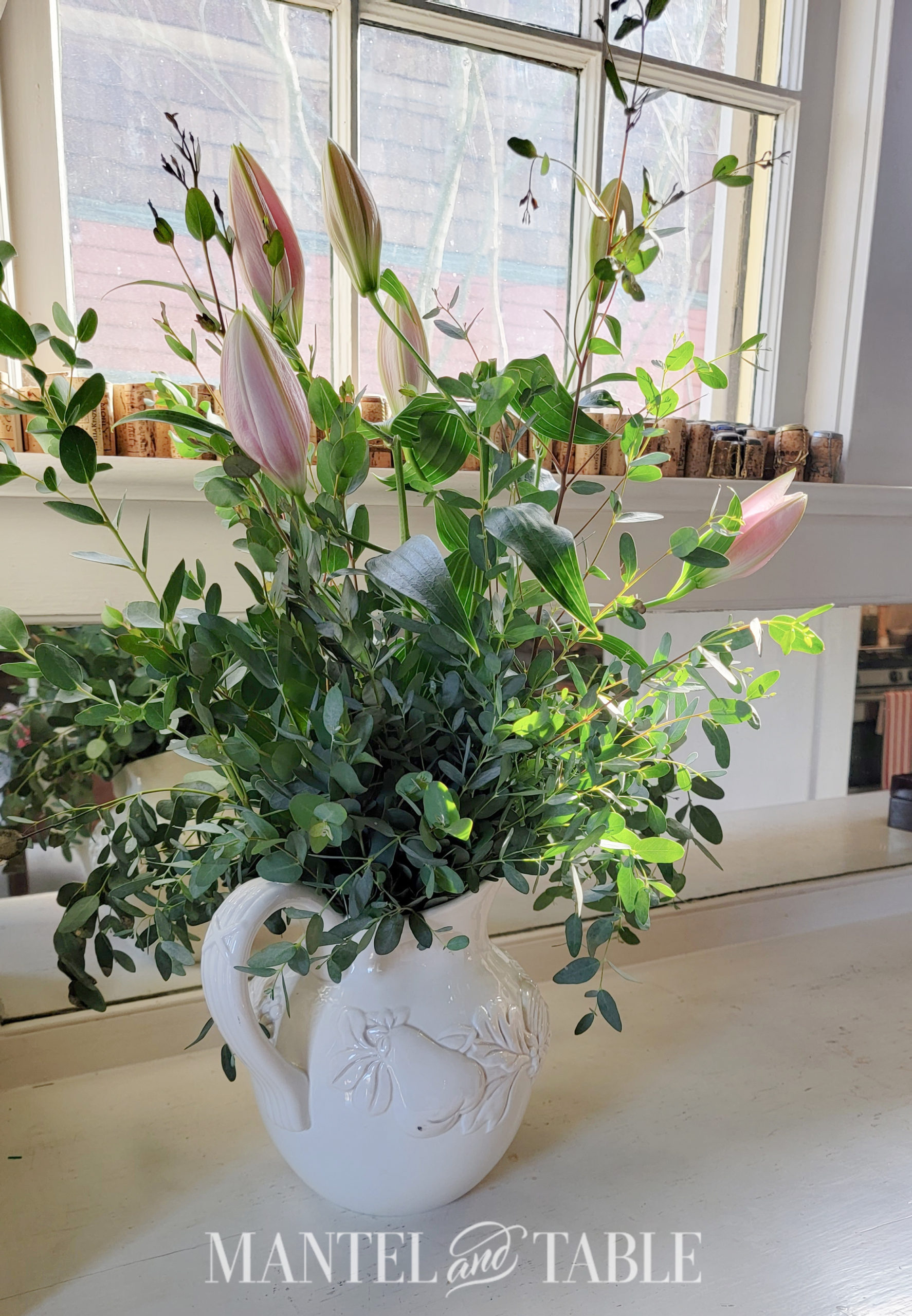 Closeup of white pitcher with greenery and lilies