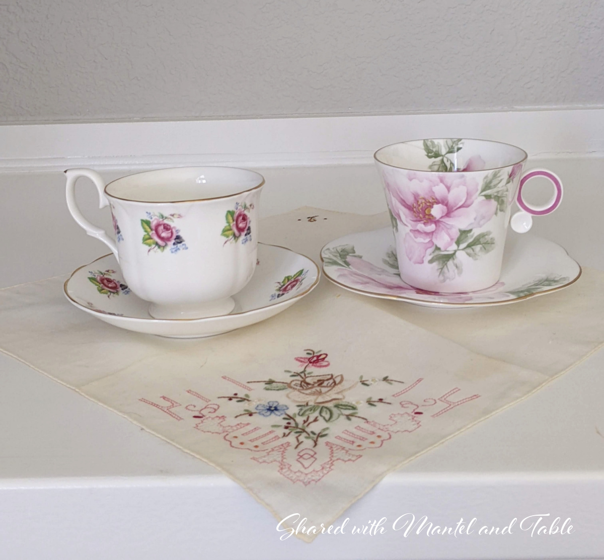 Two rose flowered teacups on an embroidered handkerchief